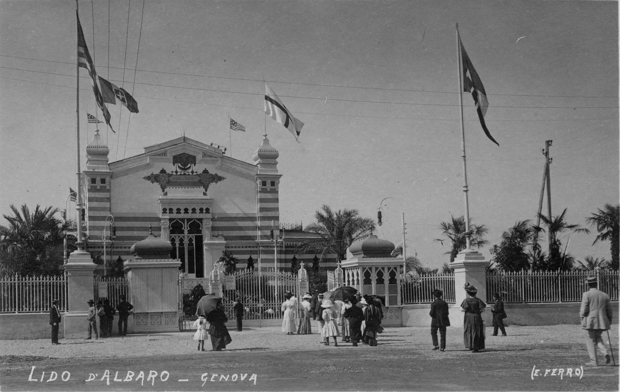Fotografia storica in bianco e nero del Lido d’Albaro a Genova, con l’edificio principale decorato, bandiere issate e persone riunite davanti all’ingresso